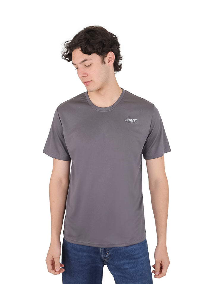 Hombre vistiendo una playera de manga corta color gris oscuro con un pequeño logo en el pecho.