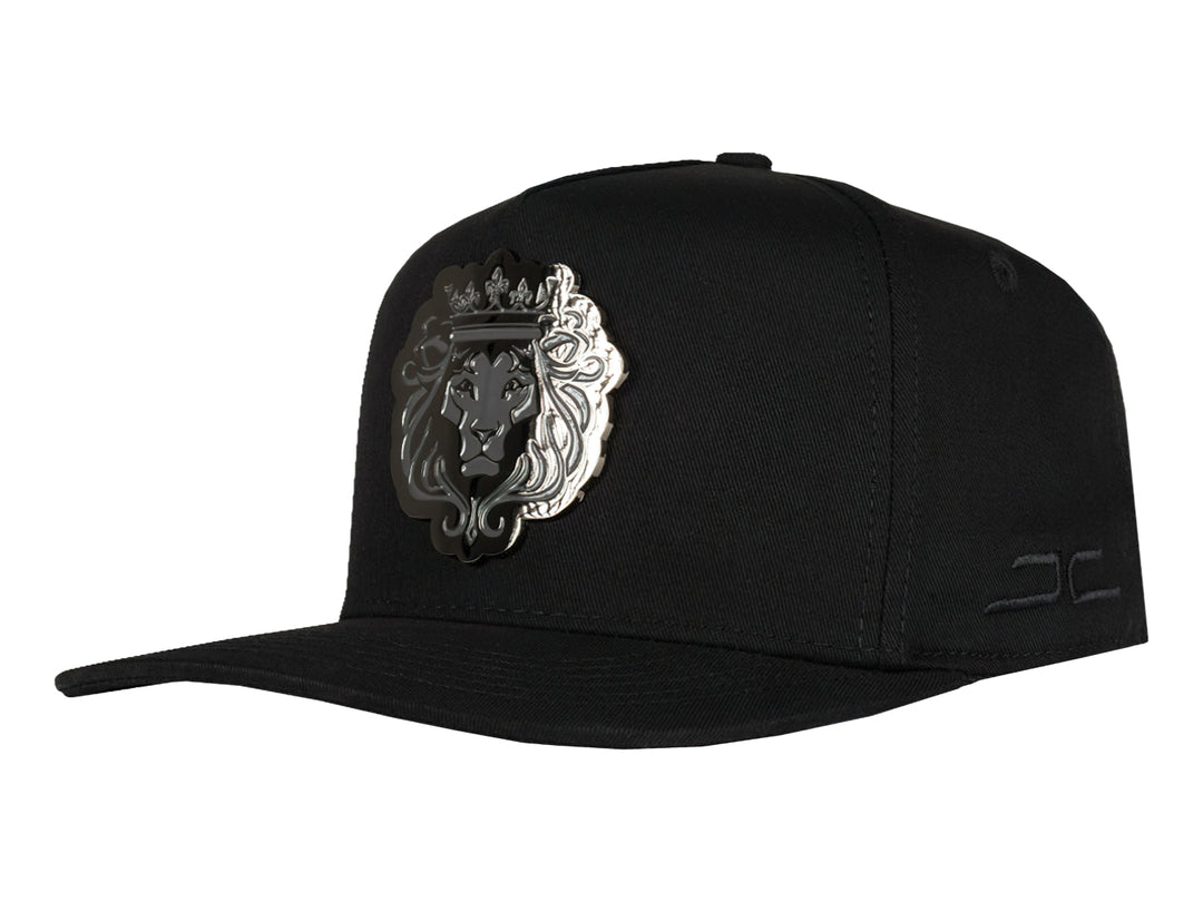 Gorra snapback color negro con un parche frontal detallado de la cabeza de un león con corona en tonos negros y grises.