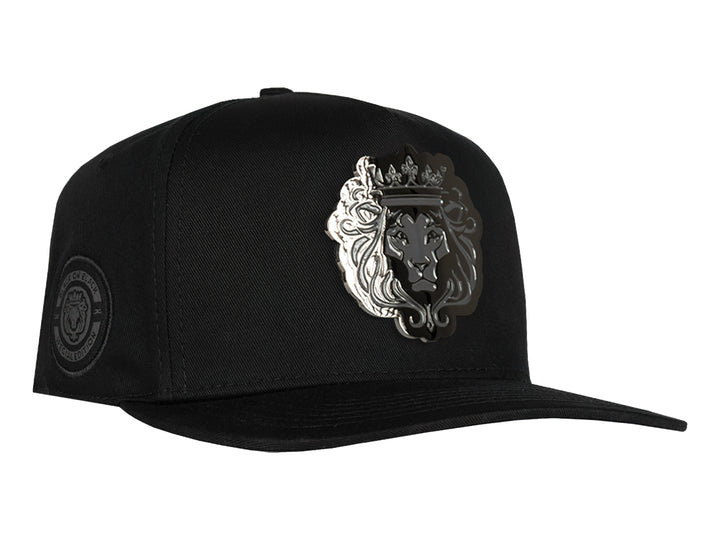 Gorra snapback color negro con un parche frontal detallado de la cabeza de un león con corona en tonos negros y grises.