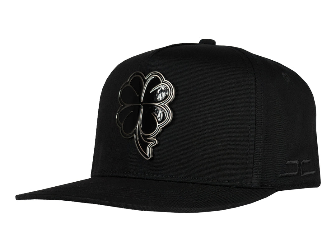 Gorra snapback color negro con un logo de trébol brillante en el frente.
