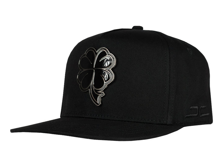 Gorra snapback color negro con un logo de trébol brillante en el frente.