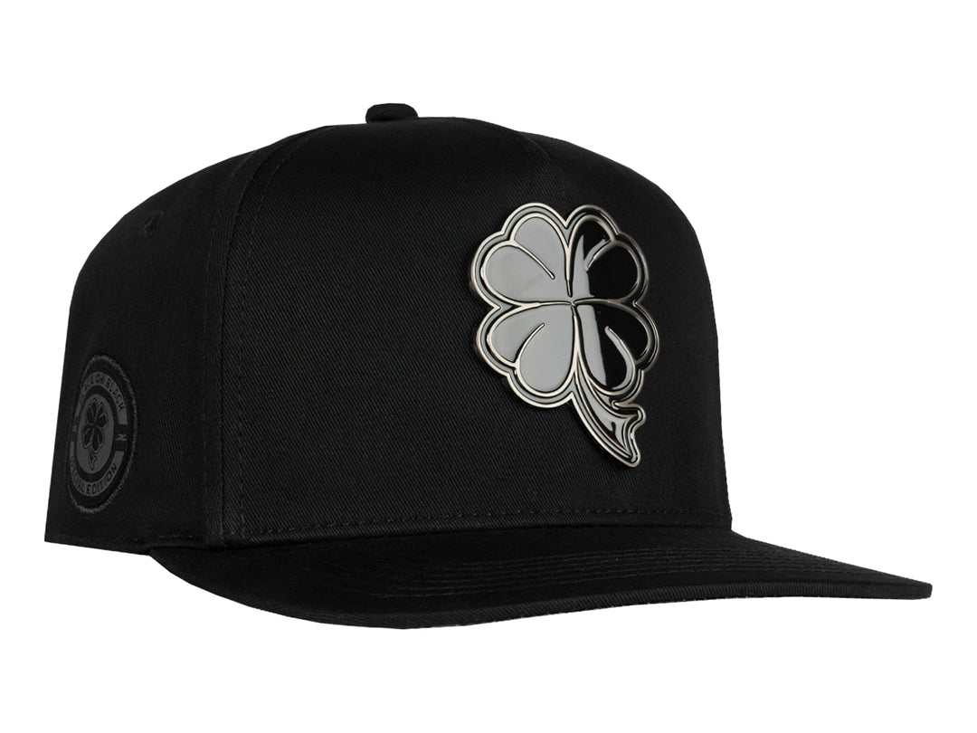 Gorra snapback color negro con un logo de trébol brillante en el frente.