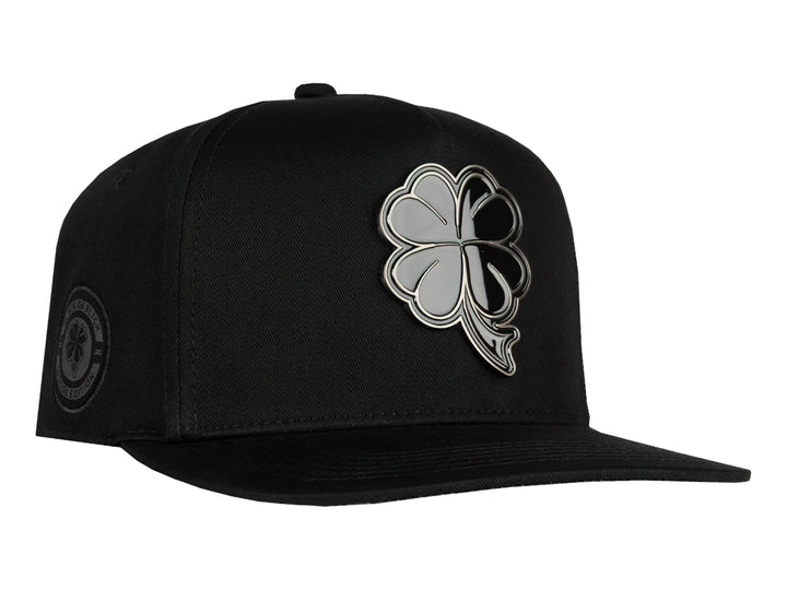 Gorra snapback color negro con un logo de trébol brillante en el frente.
