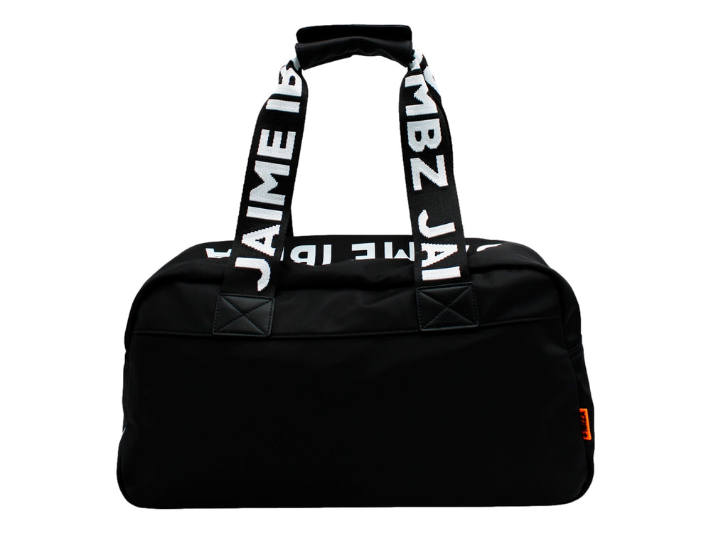 Maletín negro de Jaime Ibiza con asas anchas y un accesorio colgante color naranja, porté por una mujer.