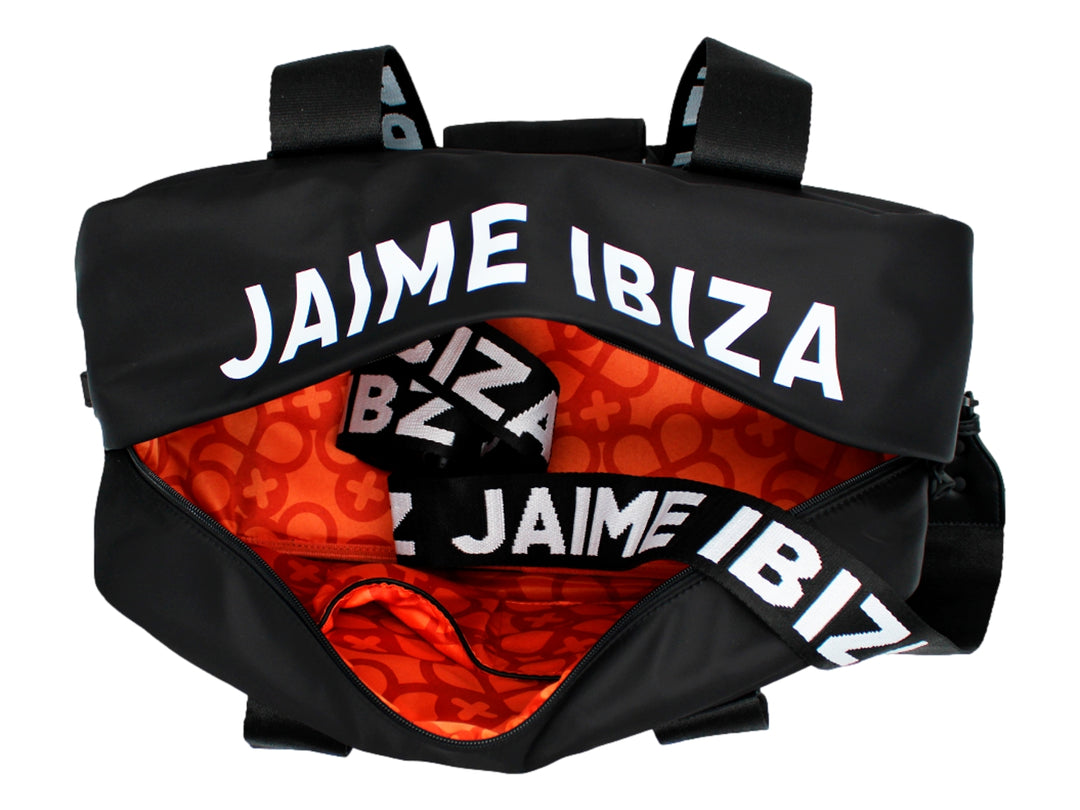 Maletín negro de Jaime Ibiza con asas anchas y un accesorio colgante color naranja, porté por una mujer.