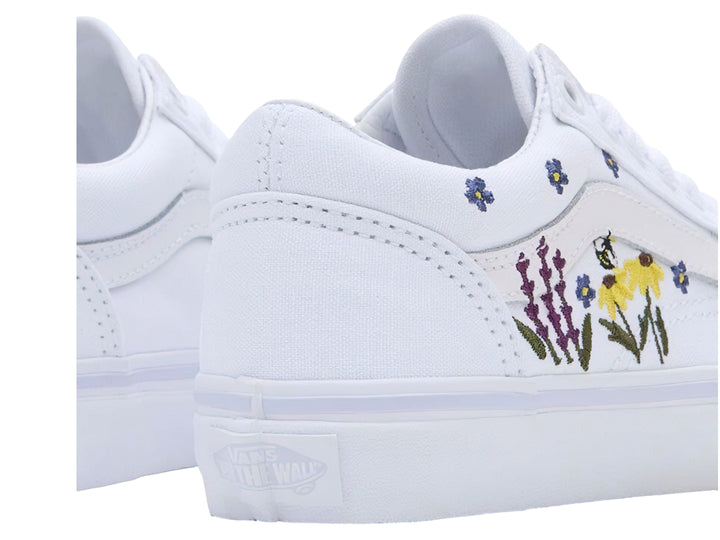 Tenis Vans blancos con bordados de flores coloridas en los laterales.