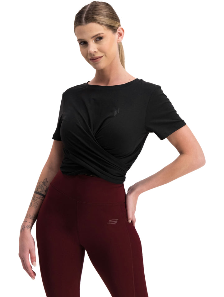 Mujer vistiendo playera deportiva negra de manga corta con diseño cruzado al frente.