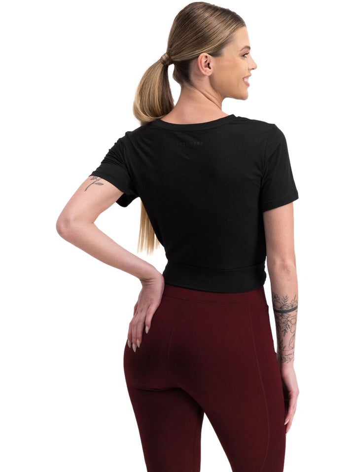 Mujer vistiendo playera deportiva negra de manga corta con diseño cruzado al frente.