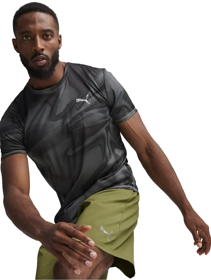 Hombre vistiendo camiseta deportiva Puma negra con estampado de puntos y shorts verdes.