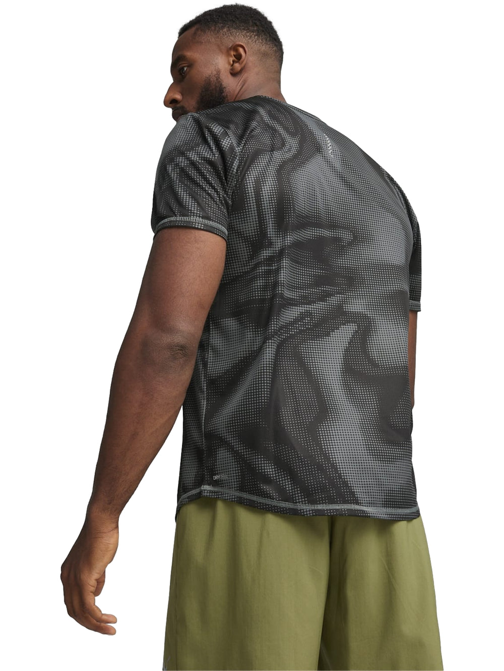Hombre vistiendo camiseta deportiva Puma negra con estampado de puntos y shorts verdes.