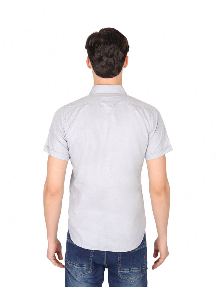 Hombre vistiendo una camisa casual de color gris con manga corta y cuello, combinada con jeans azules.