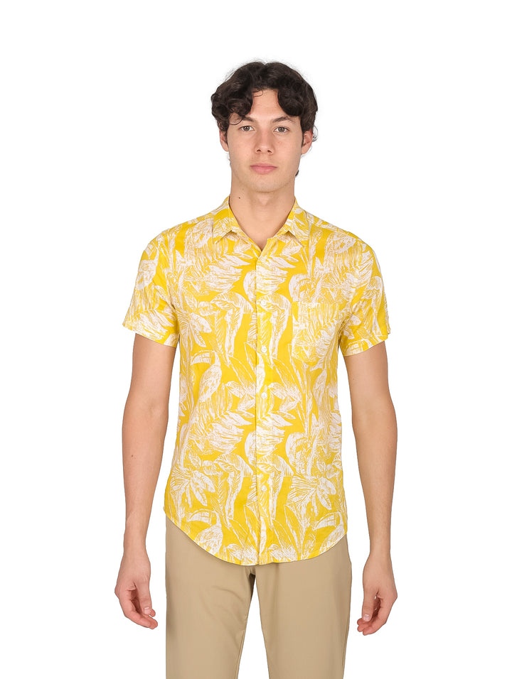 Hombre vistiendo camisa amarilla de manga corta con estampado de hojas blancas.