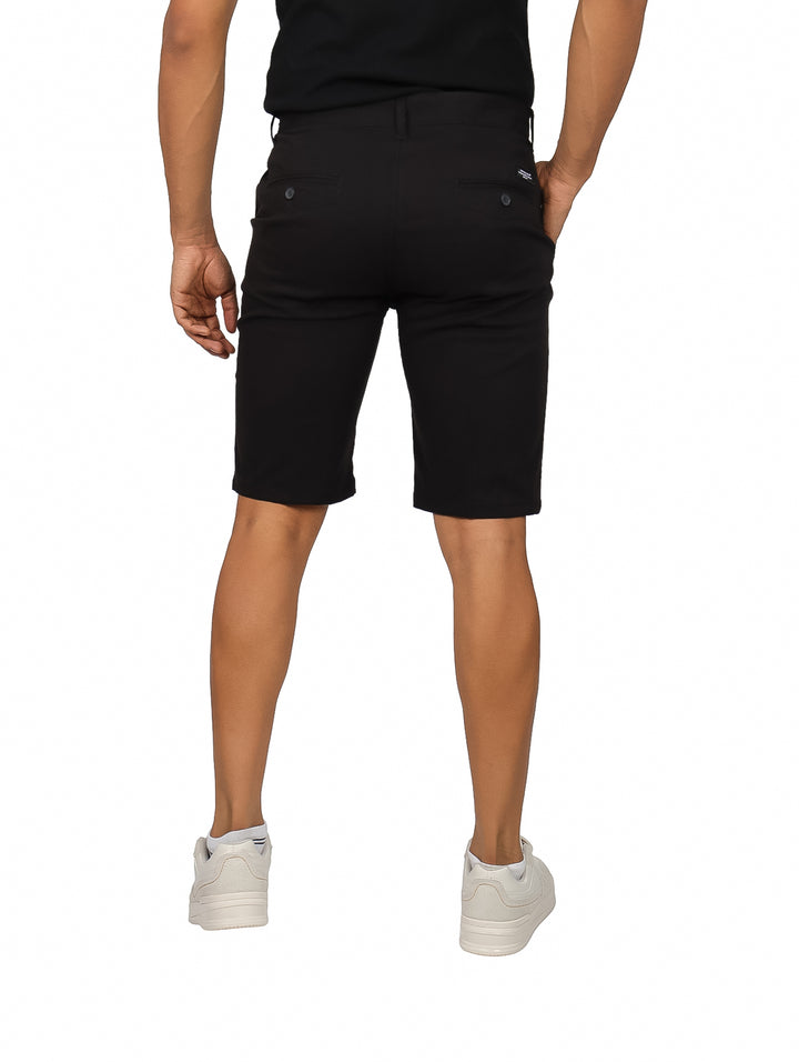 Hombre vistiendo bermudas color negro de corte casual con calzado blanco sobre fondo blanco.