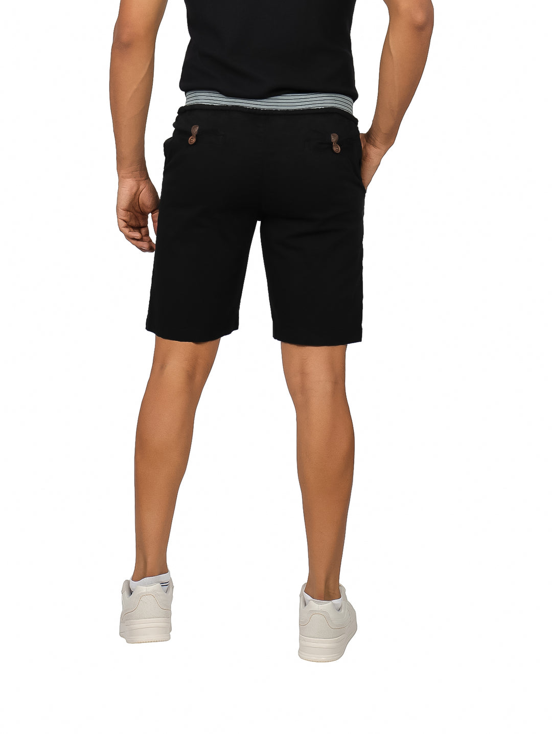 Hombre vistiendo bermudas negras casuales con cinturón a rayas y tenis blancos.