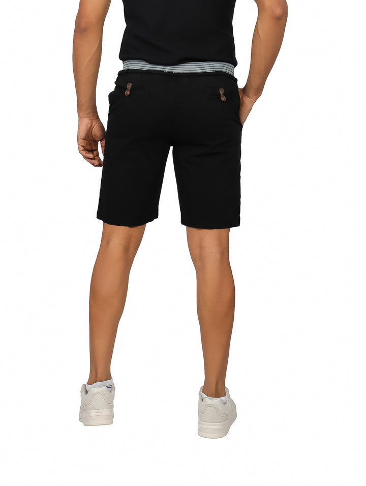 Hombre vistiendo bermudas negras casuales con cinturón a rayas y tenis blancos.