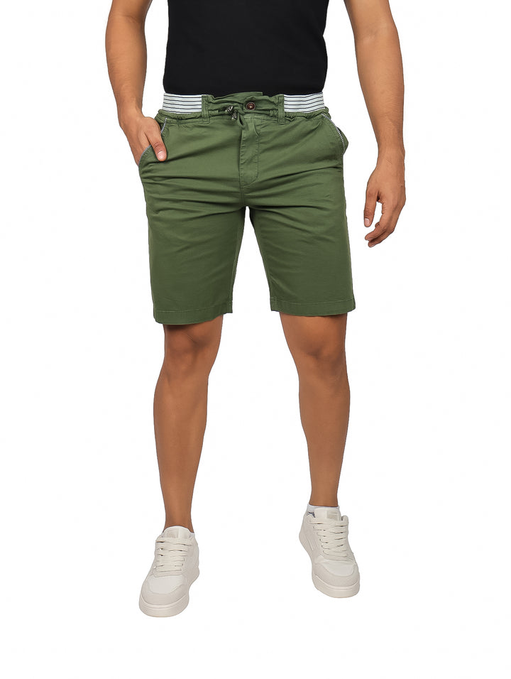 Hombre vistiendo bermudas color olivo con cintura elástica y tenis blancos.
