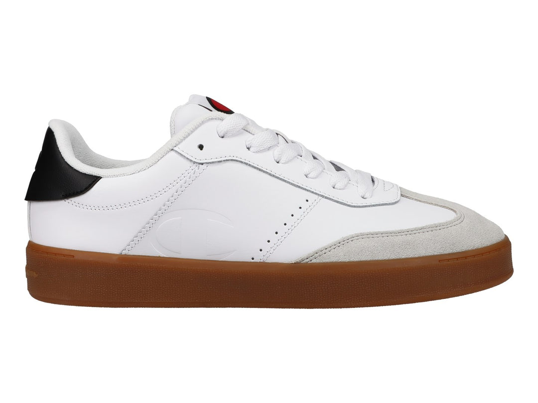 Tenis Champion blancos con suela de goma color café, punta gris y detalle negro en el talón.