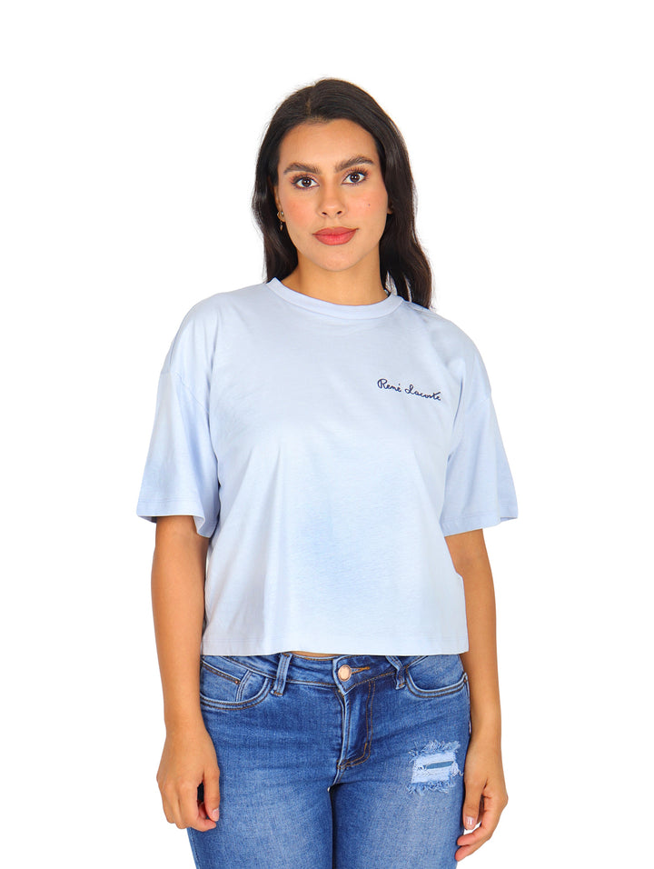 Mujer vistiendo una camiseta Lacoste de color azul claro con corte boxy y cuello redondo.