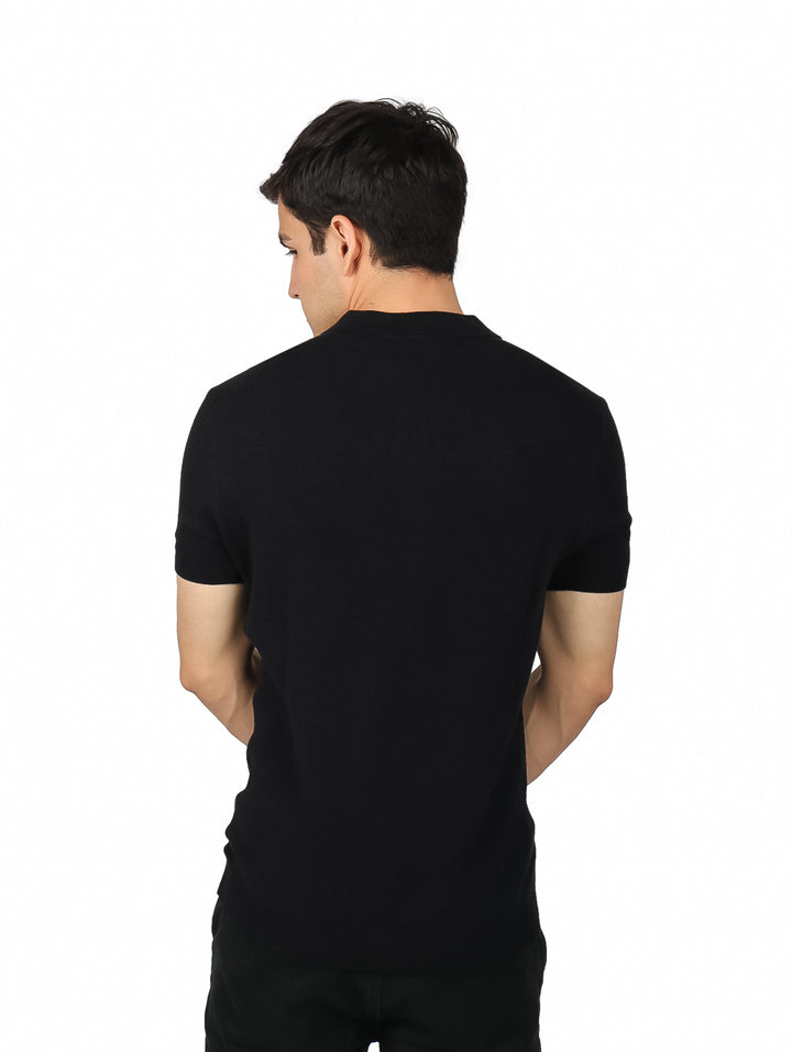 Hombre vistiendo una playera tipo polo de color negro, manga corta y cuello con botones sobre fondo blanco.