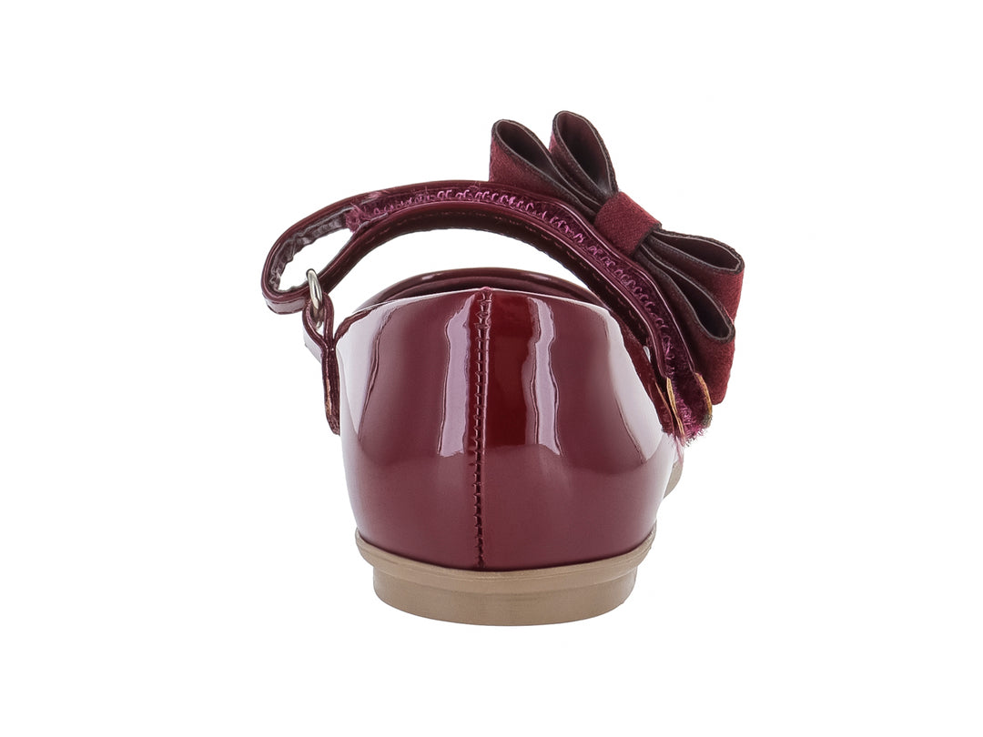 Zapato plano de charol color vino con moño adornado con brillantes y suela beige.