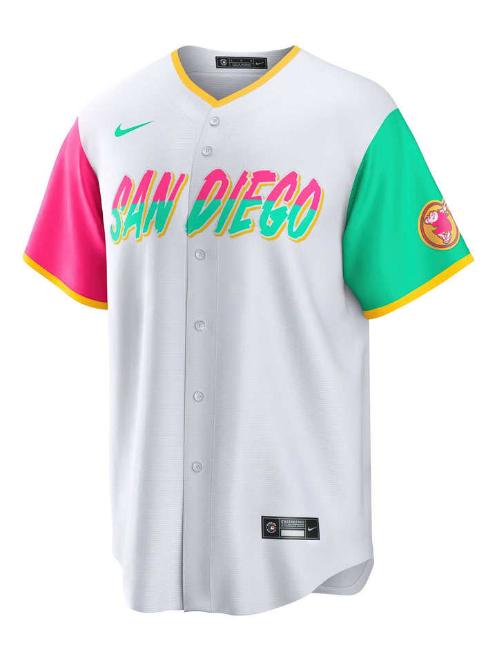 Jersey de béisbol Nike San Diego Padres blanco con mangas rosa y verde y letras multicolores en el pecho.