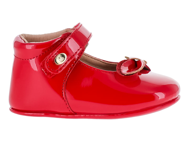 Zapato infantil color rojo brillante con acabado de charol, correa ajustable y moño decorativo.