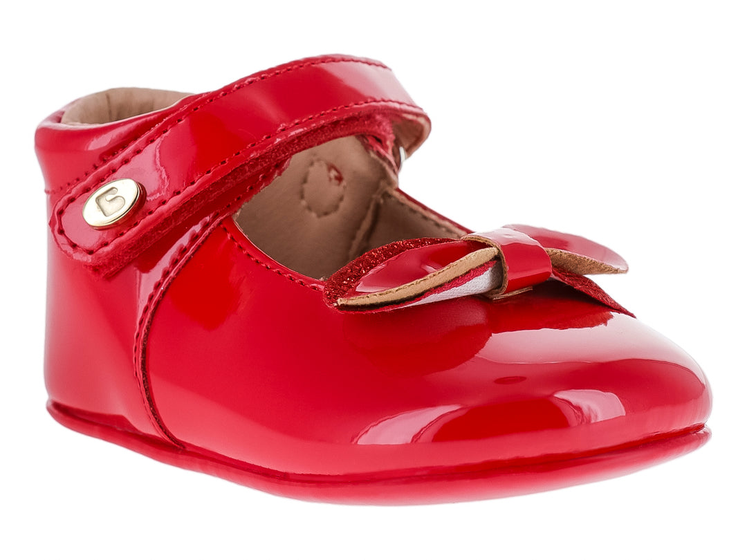 Zapato infantil color rojo brillante con acabado de charol, correa ajustable y moño decorativo.