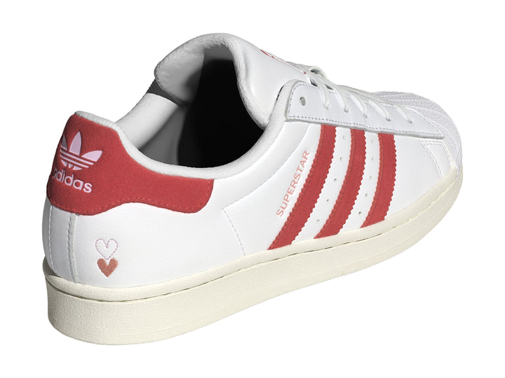 Tenis Adidas Superstar blancos con tres franjas rojas laterales y detalle rojo en el talón.