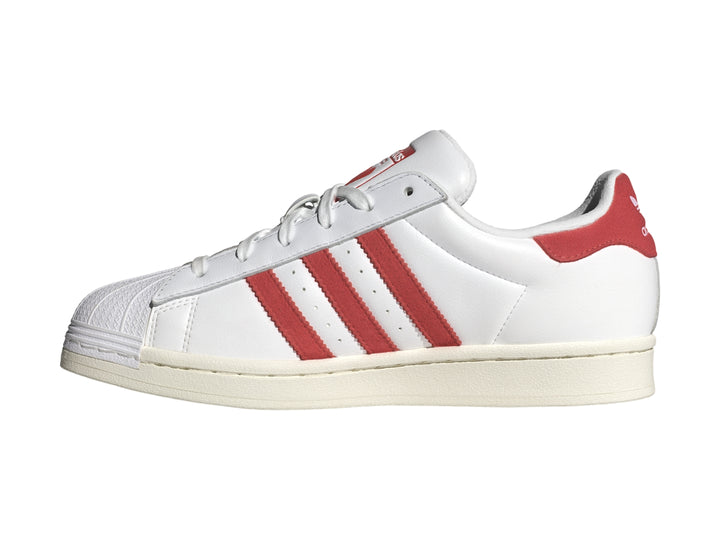 Tenis Adidas Superstar blancos con tres franjas rojas laterales y detalle rojo en el talón.