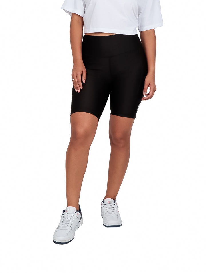 Mujer vistiendo shorts biker color negro de cintura alta y tenis blancos.