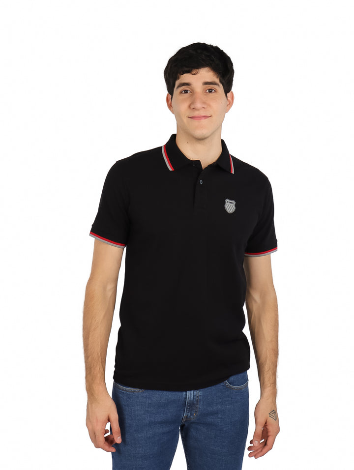 Hombre vistiendo playera polo K-SWISS color negro con detalles rojos y blancos en el cuello y mangas.