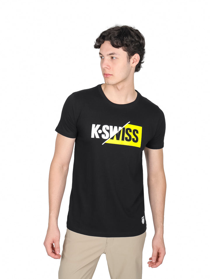 Hombre vistiendo playera K-Swiss de color negro con logotipo estampado en el pecho en colores blanco y amarillo.
