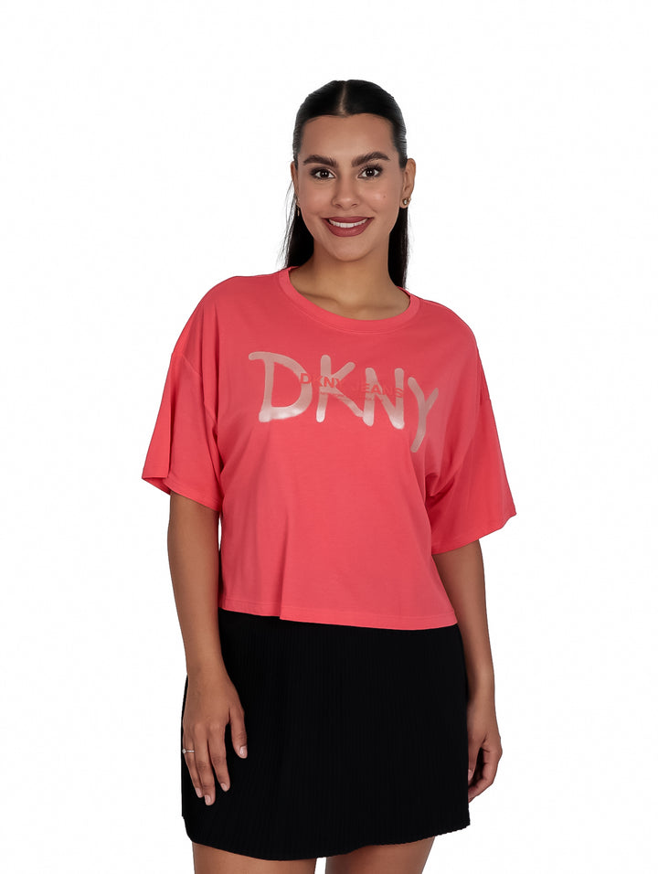 Mujer vistiendo camiseta corta color coral con logo DKNY en dorado y falda negra.