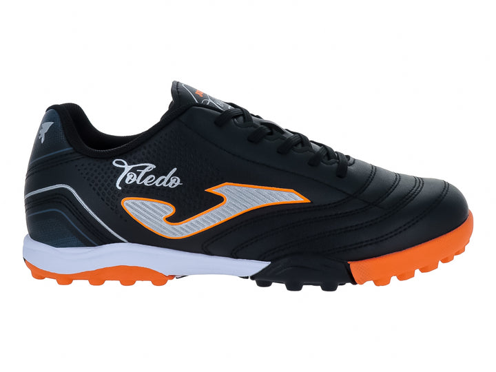 Zapato de fútbol Joma Toledo JR color negro con detalles en naranja y blanco y suela para césped artificial.