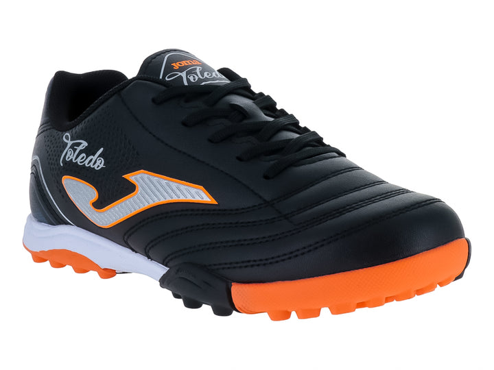 Zapato de fútbol Joma Toledo JR color negro con detalles en naranja y blanco y suela para césped artificial.