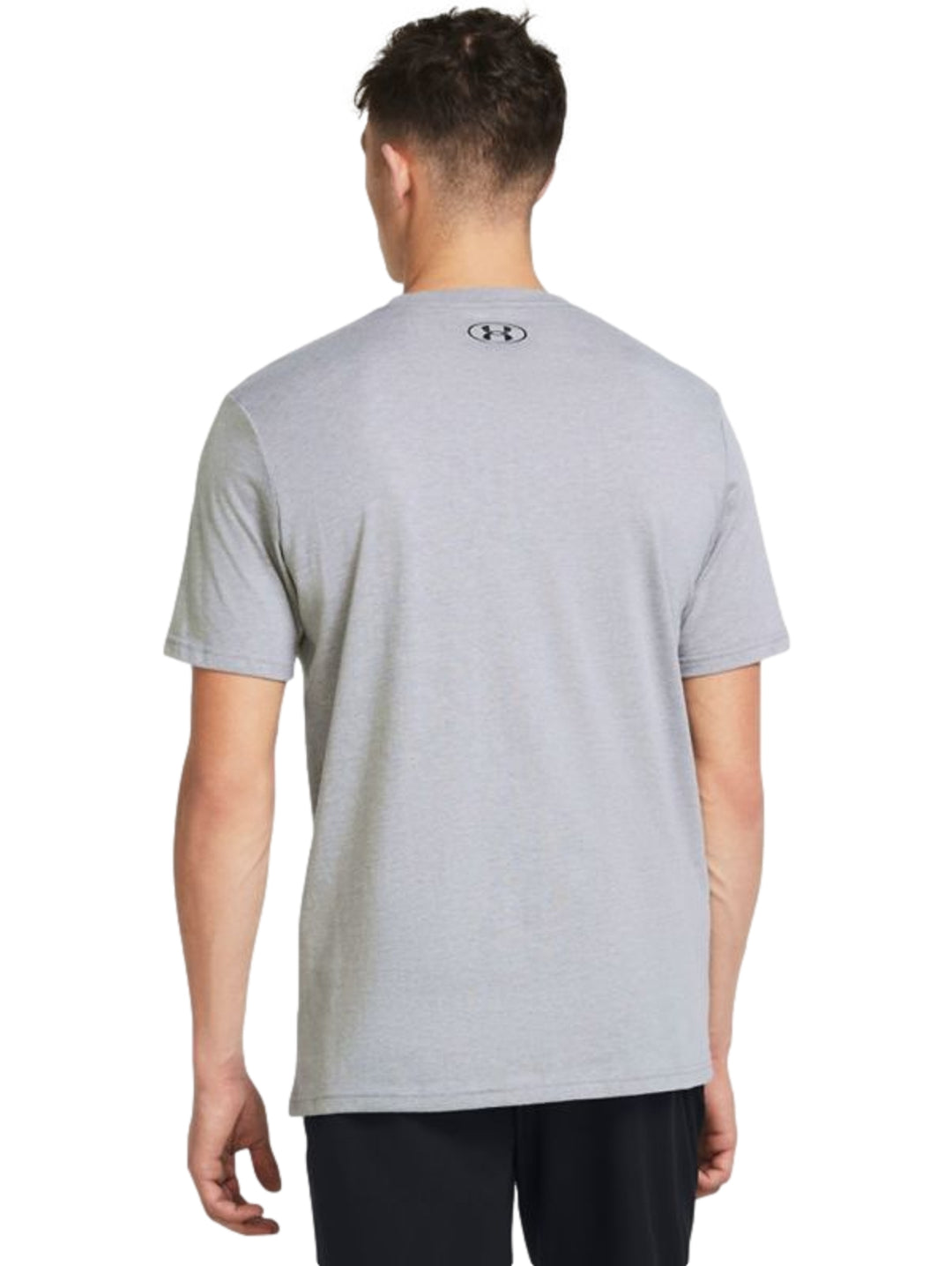 Hombre vistiendo una playera deportiva de color gris con el logotipo de Under Armour en negro en el pecho.