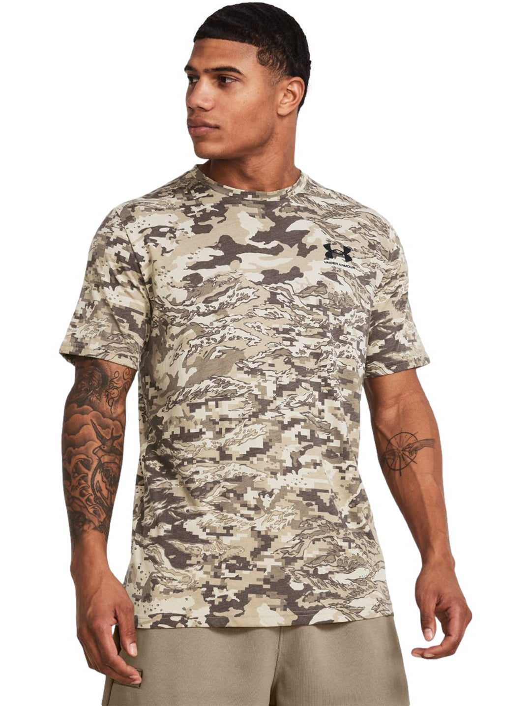 Hombre vistiendo camiseta Under Armour de manga corta con estampado de camuflaje en tonos marrón y beige.