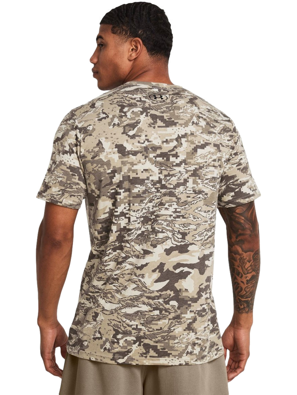 Hombre vistiendo camiseta Under Armour de manga corta con estampado de camuflaje en tonos marrón y beige.