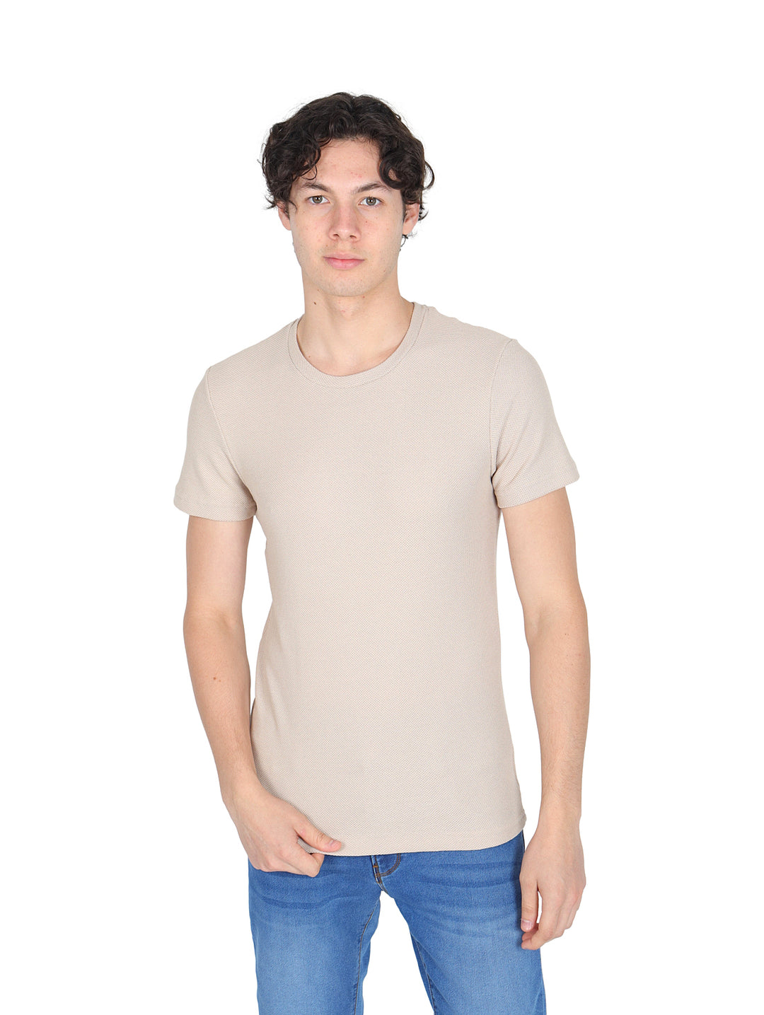 Hombre vistiendo una playera de manga corta color beige con cuello redondo y jeans azules sobre fondo blanco.