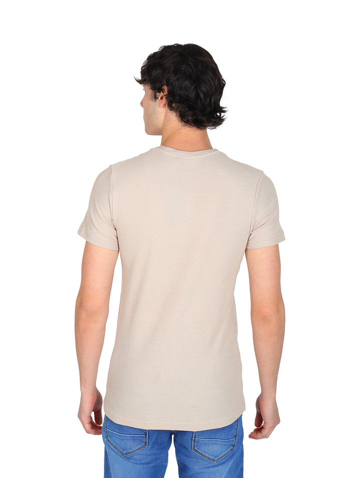 Hombre vistiendo una playera de manga corta color beige con cuello redondo y jeans azules sobre fondo blanco.