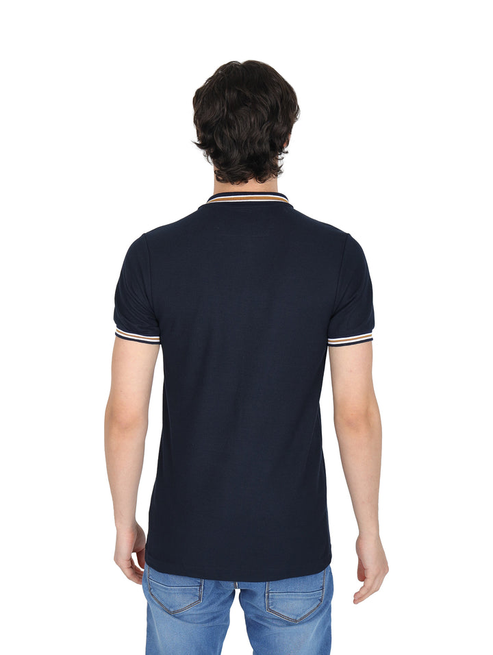 Hombre vistiendo playera polo color marino con detalles de rayas blancas y beige en el cuello y mangas.