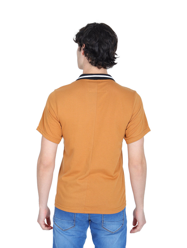 Hombre vistiendo playera polo color ocre con cuello negro y pantalones azules.