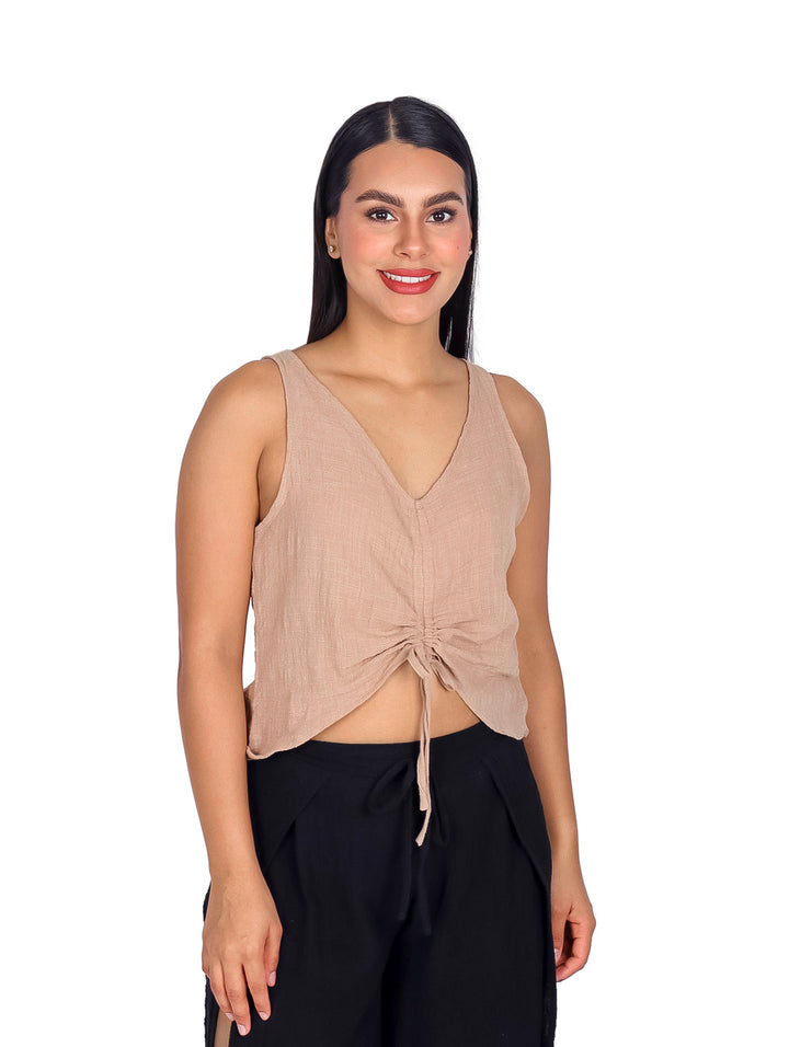 Mujer vistiendo blusa color arena sin mangas con detalle de surcido frontal y pantalones negros.