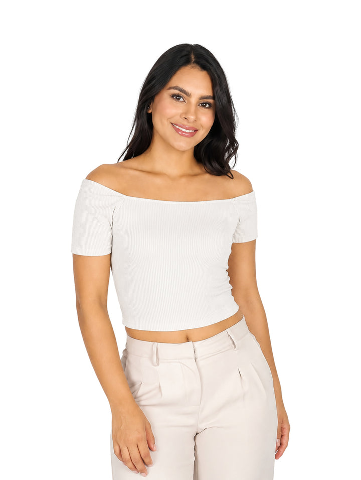 Mujer vistiendo blusa beige de hombros descubiertos y pantalones a juego sobre fondo blanco.
