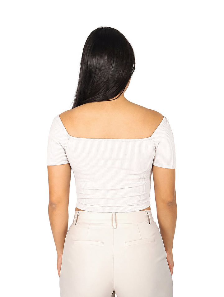 Mujer vistiendo blusa beige de hombros descubiertos y pantalones a juego sobre fondo blanco.