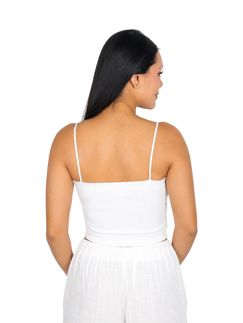 Mujer vistiendo blusa blanca corta de tirantes y pantalones blancos sobre fondo blanco.