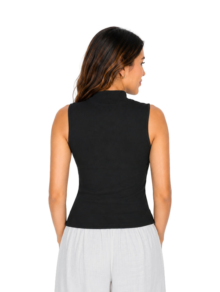 Mujer vistiendo blusa negra sin mangas con abertura en el cuello y pantalones blancos.