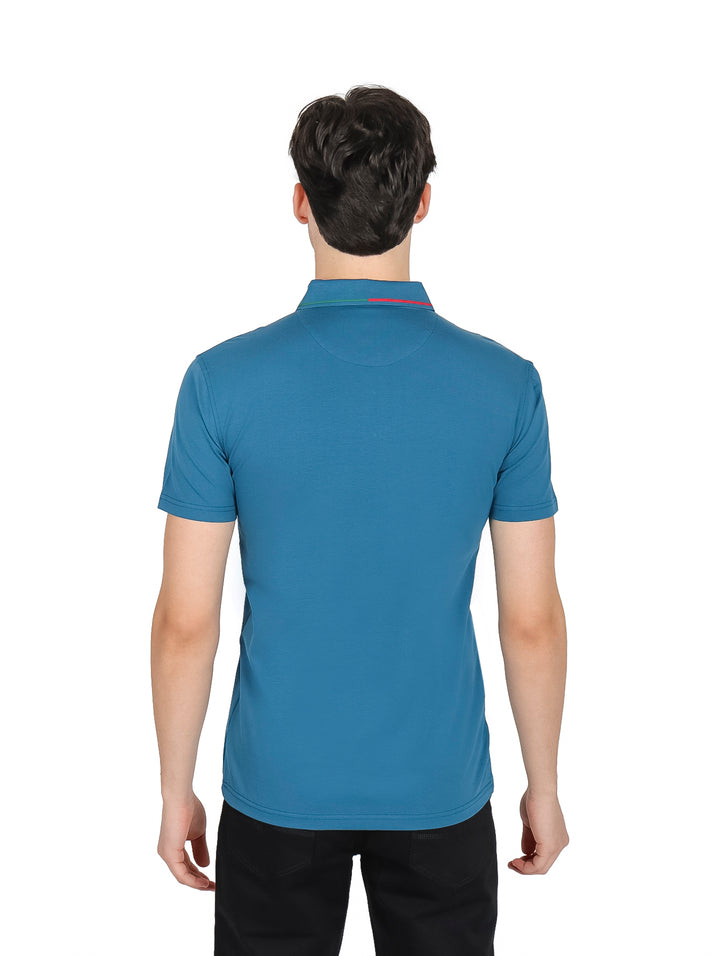Hombre vistiendo una playera polo color teal con detalles en rojo y verde en el cuello y pechera.
