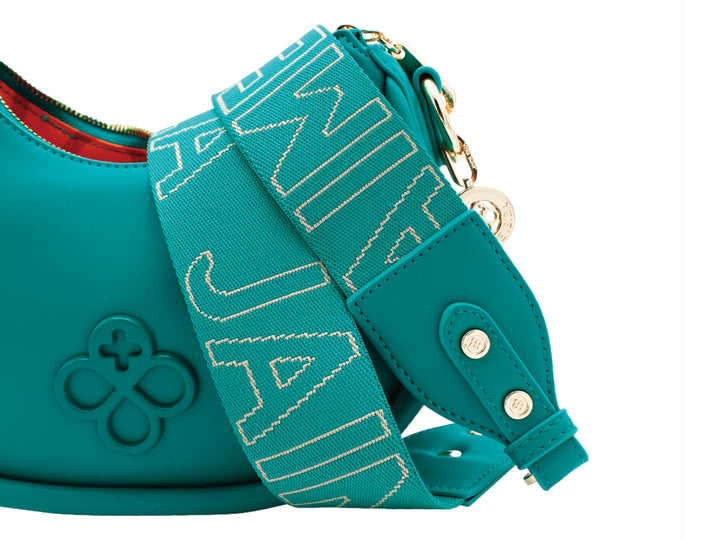 Bolso de mano color turquesa con forma de media luna, correa ajustable y detalles metálicos en dorado.