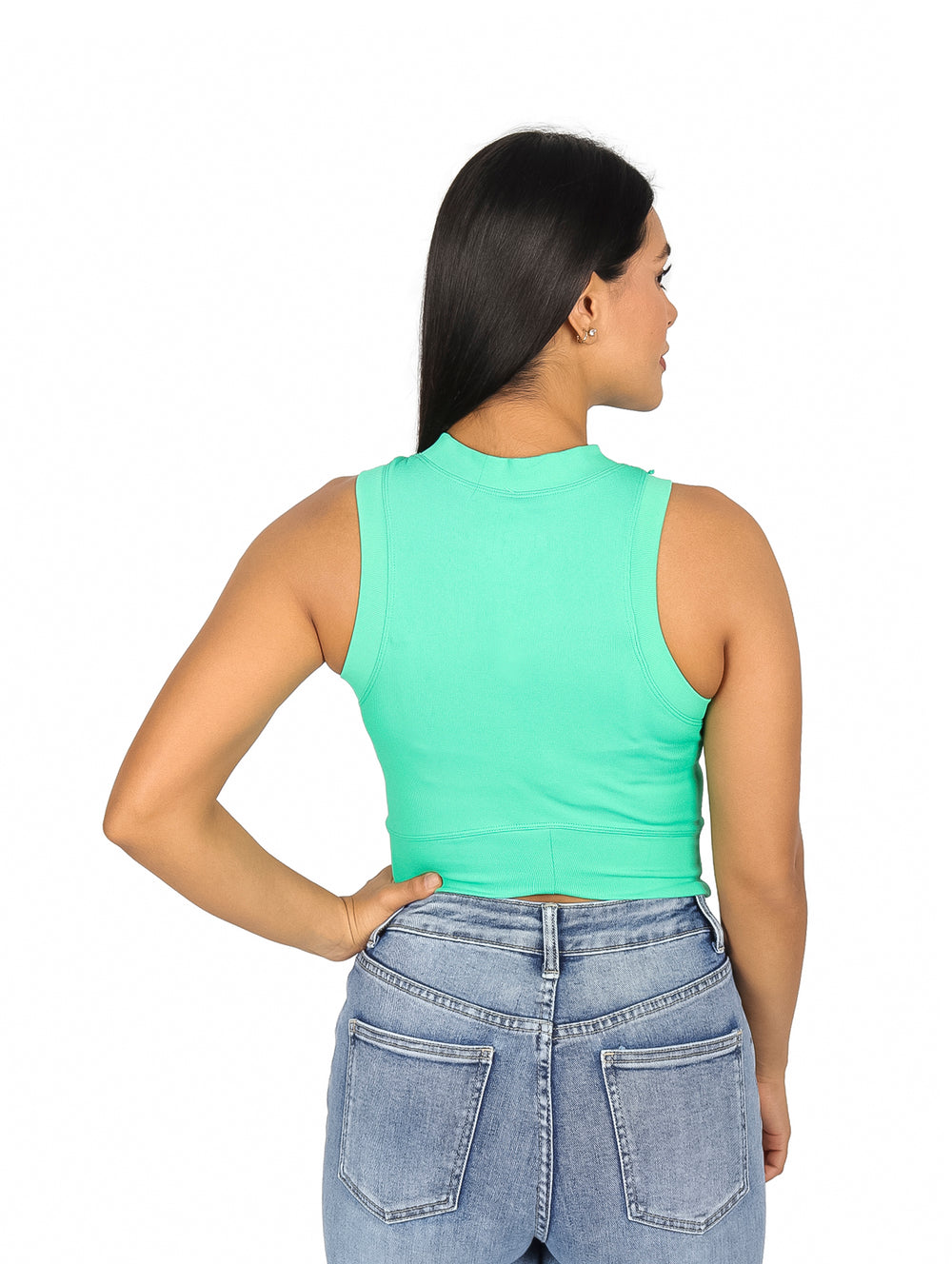 Mujer usando un top verde sin mangas y jeans azules sobre fondo blanco.